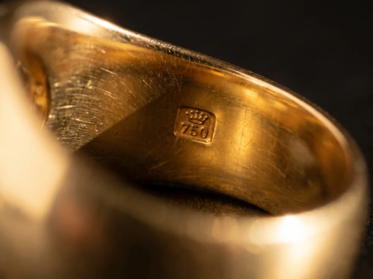 A macro photograph of a 750 hallmark stamped inside a gold ring band.